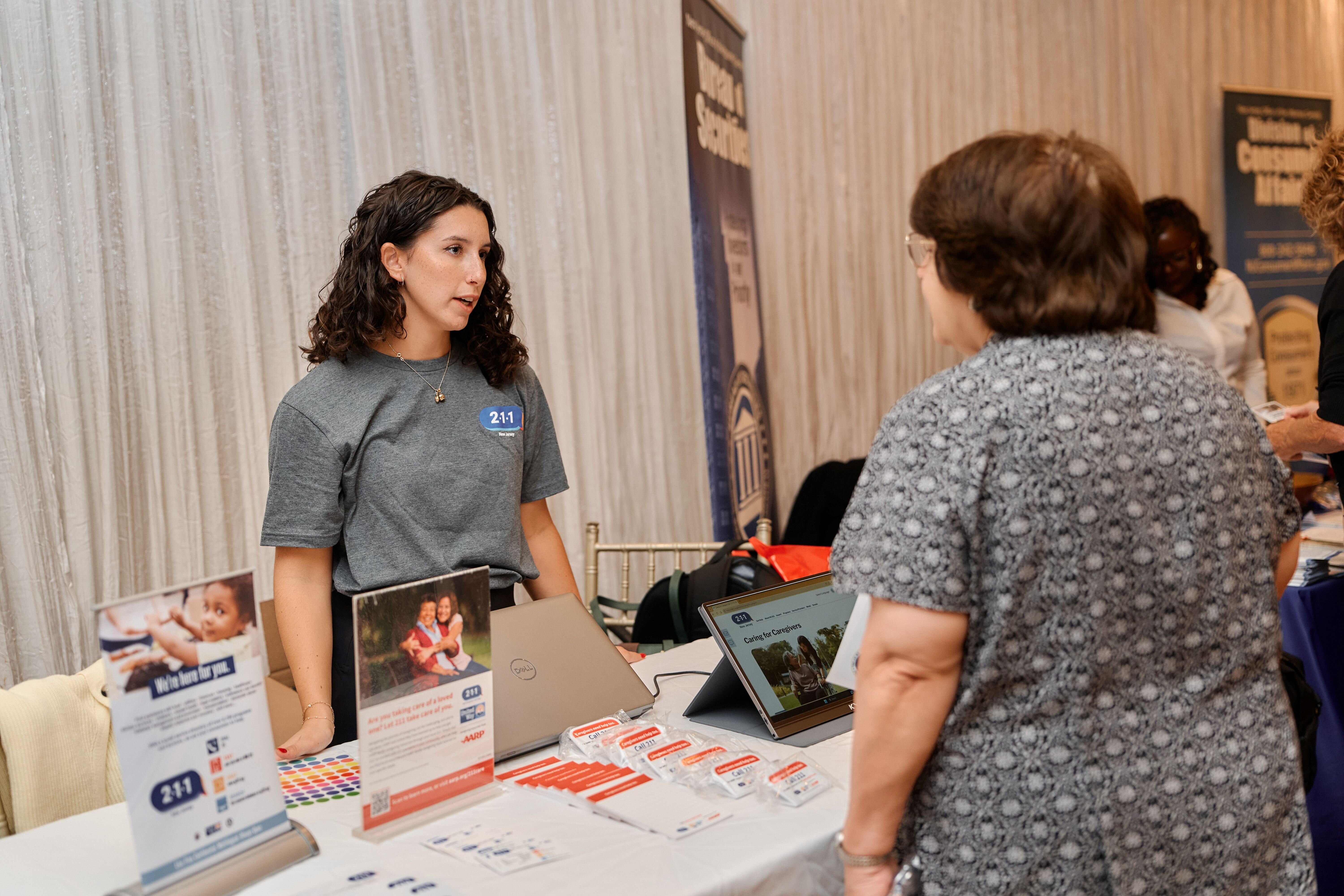 woman stands at information table speaking to another woman