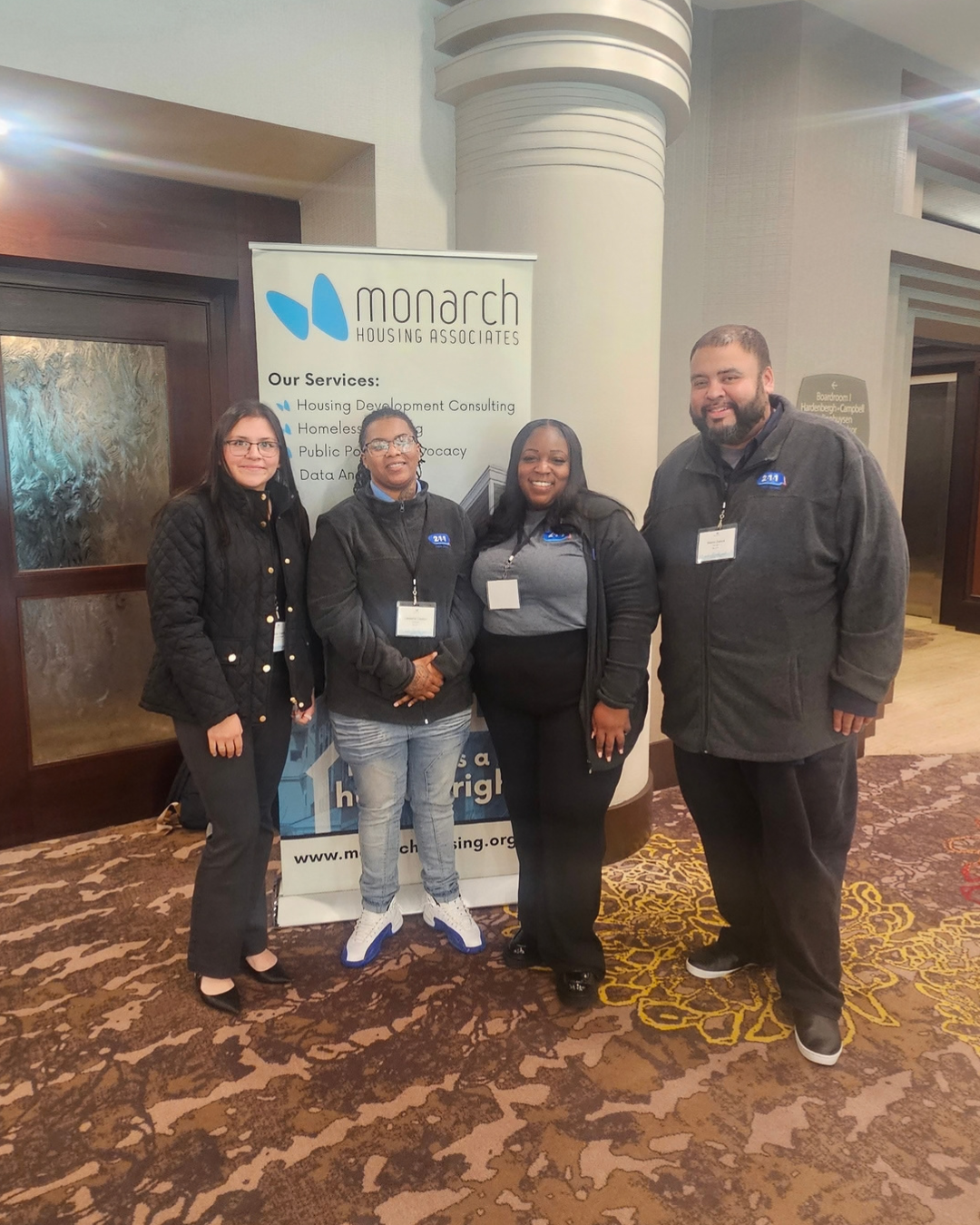 four people standing in front of a sign at a convention